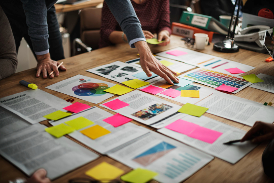 People collaborating around a table covered with documents, charts, and colorful sticky notes for planning. This strategy gives your calendar structure and diversity.